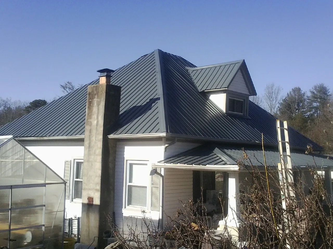 Dark blue standing seam metal roof on a white farmhouse with dormer — Slate & Tile Roof Repair by Roofing Brothers in East Leroy