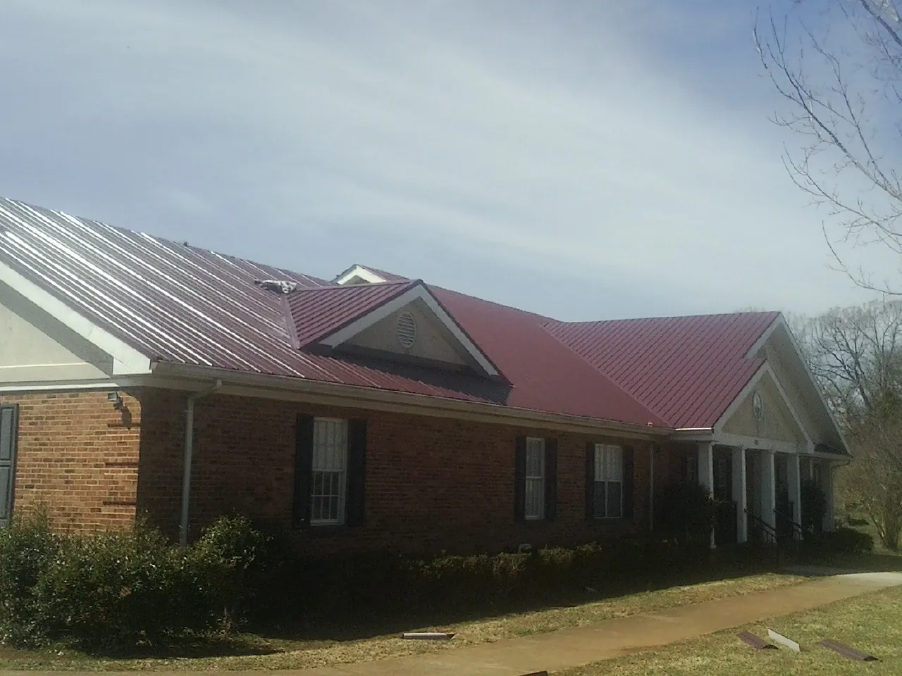 Red metal roof with gabled entries on a long brick building, from a Hail Damage Roof Repair job in East Leroy