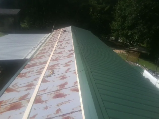 Old rusted panels beside newly installed green metal roofing — Wind Damage Roof Repair by Roofing Brothers in East Leroy