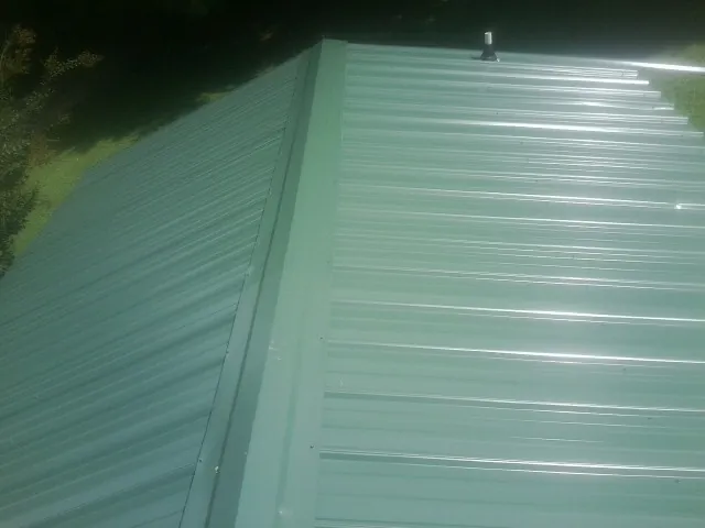 New green metal panels meeting at the ridge of a roof — Flat Roof Repair work by our crew in East Leroy