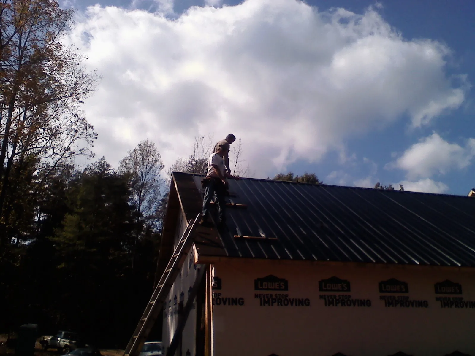 Roofer fastening dark metal panels high against a cloudy sky, from a Roof Inspection job in East Leroy