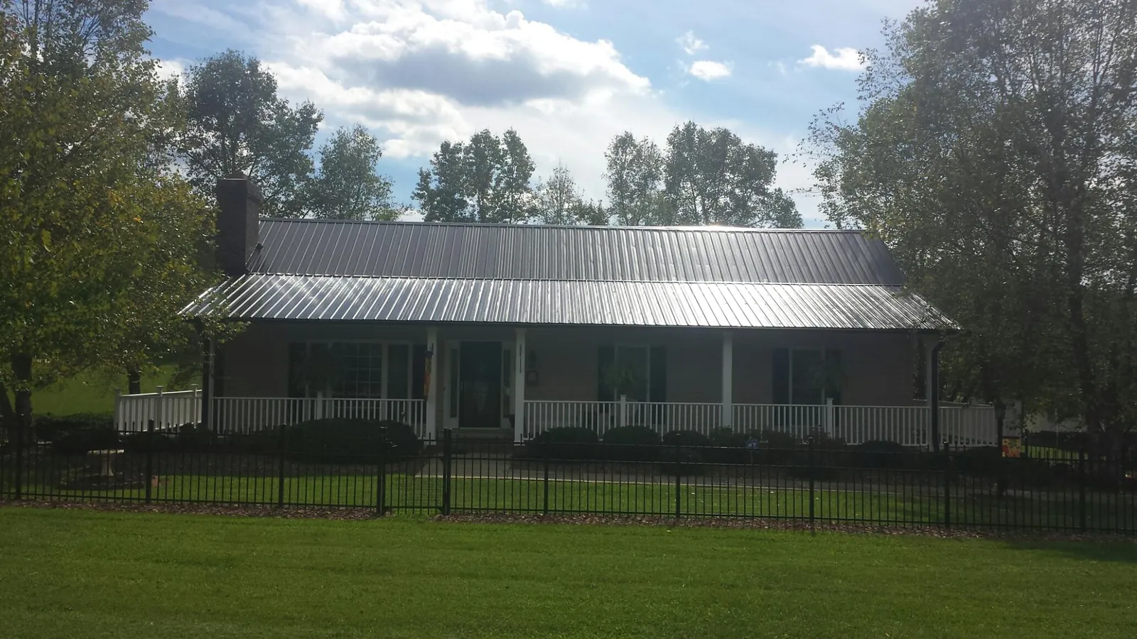 Gray metal roof on a brick ranch with a full width front porch — Gutter Guard Installation work by our crew in East Leroy
