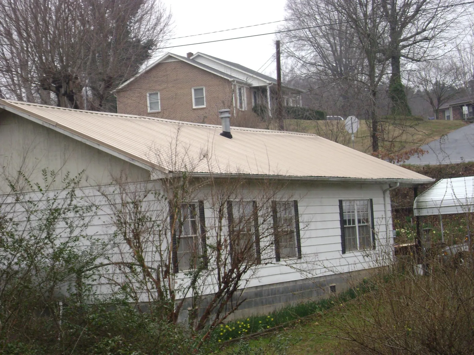 Tan metal roof on a white sided house set into a hillside — Commercial Roofing by Roofing Brothers in East Leroy