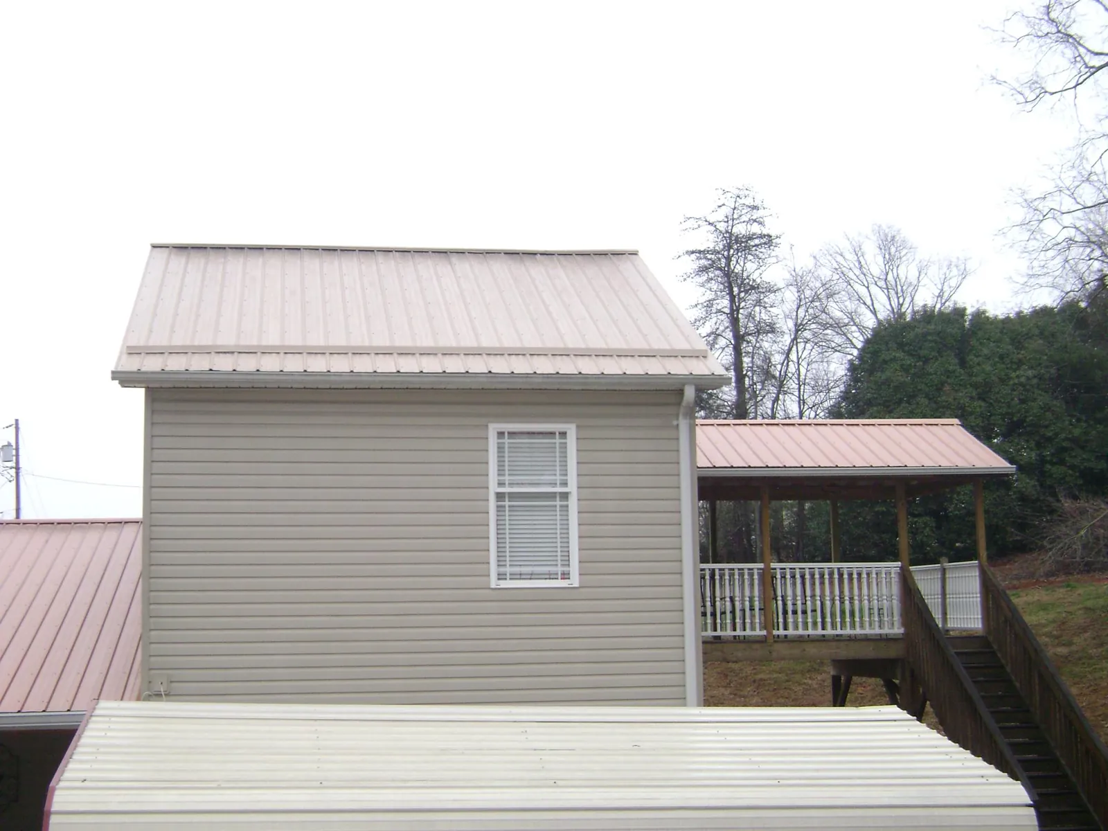 Tan metal roofs on a two story addition and attached porch, from a Roof Replacement job in East Leroy